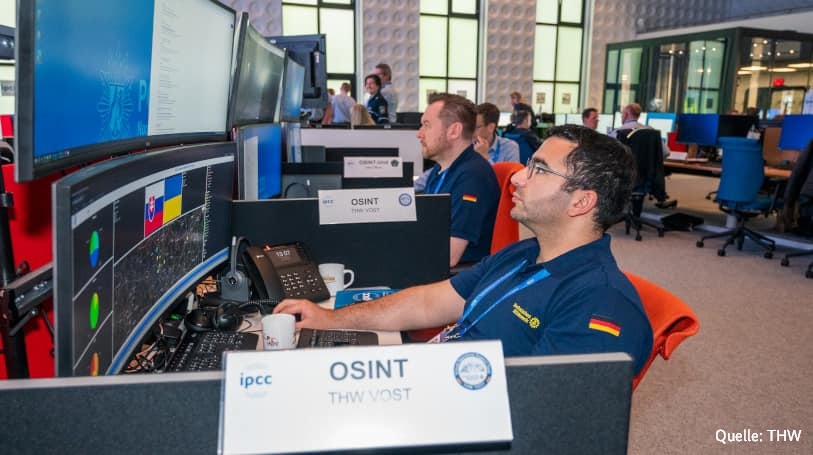 Auf dem Foto sieht man im Vordergrund zwei Einsatzkräfte des Virtual Operations Support Team, die vor großen Bildschirmen mit Computern arbeiten.
